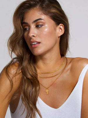 Gold layered necklace with a herringbone chain and a cross pendant.