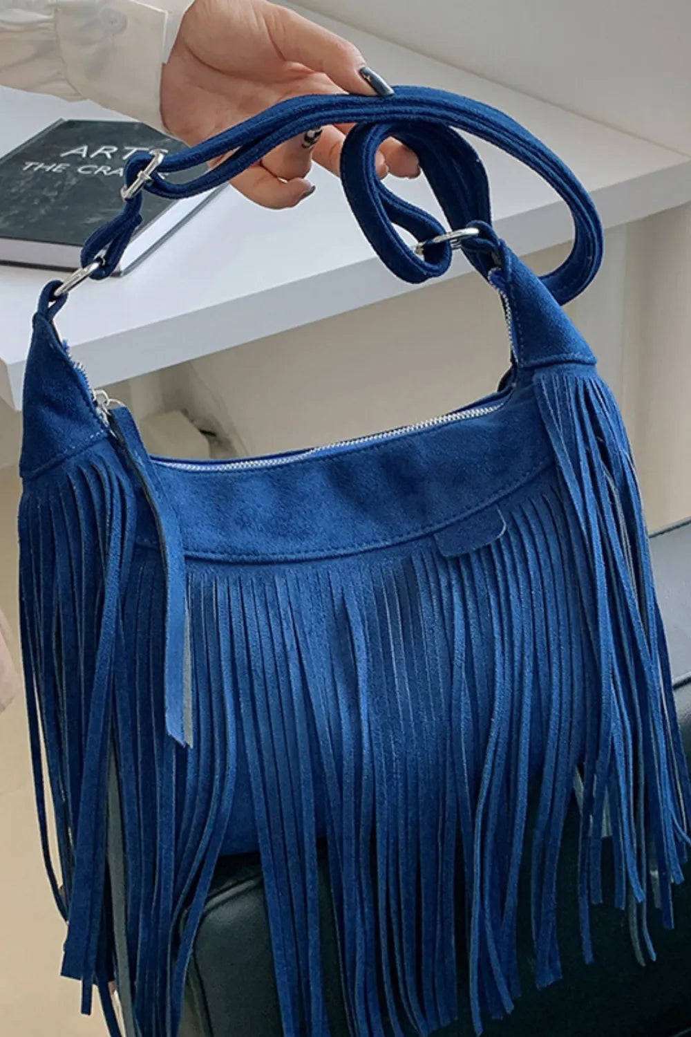 Blue suede crescent crossbody bag with fringe detail and adjustable strap.