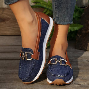 Blue denim slip-on loafers with brown trim and gold buckle detail.