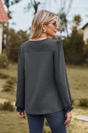 Dark gray waffle knit blouse with perforated details and ruffled cuffs.