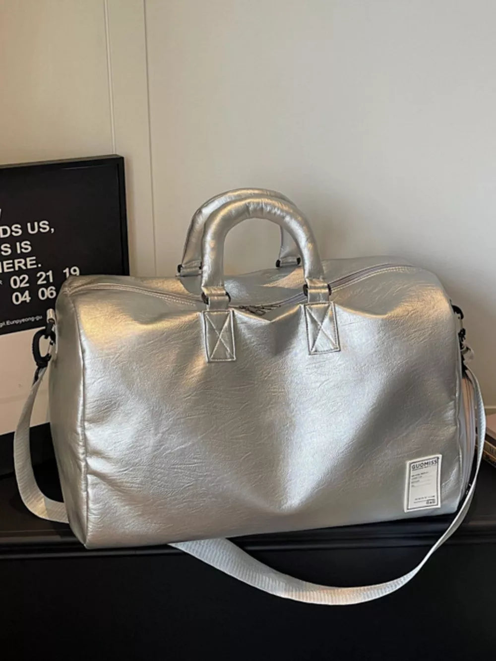 Spacious silver pu leather travel duffel bag with top handles and shoulder strap.