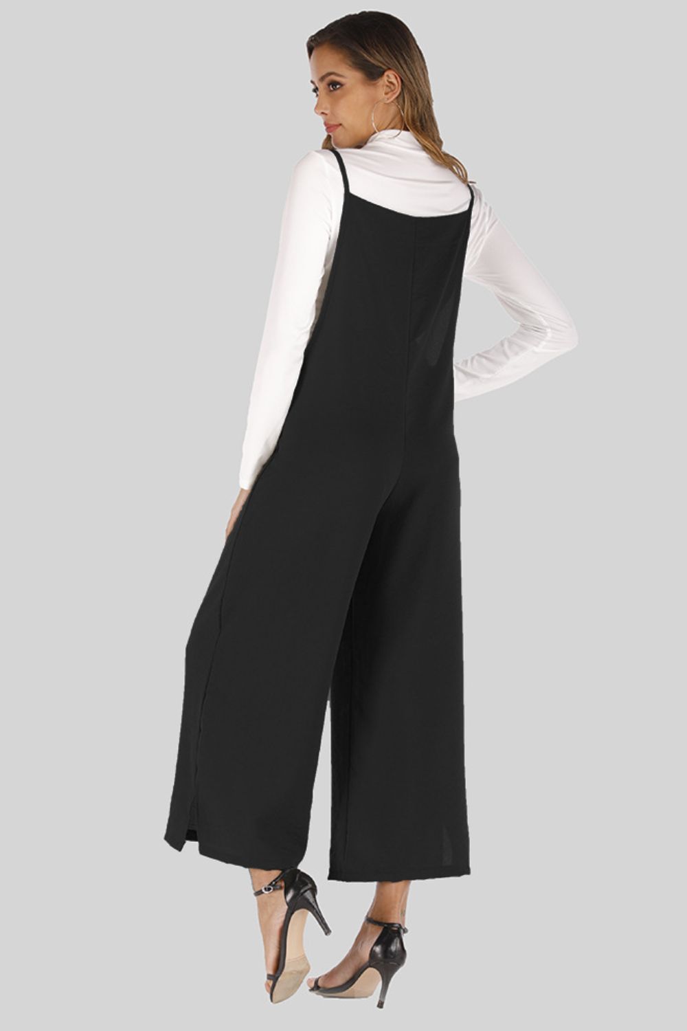 Black culotte overalls with slender straps and wide legs, styled over a white long-sleeve top.