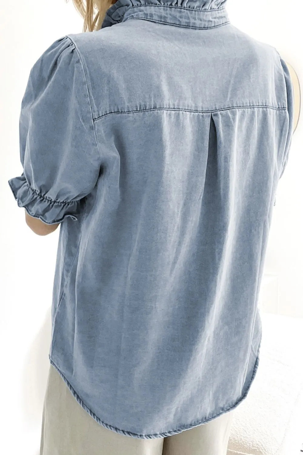Light blue denim blouse with ruffled collar, puff sleeves, and button front detail.