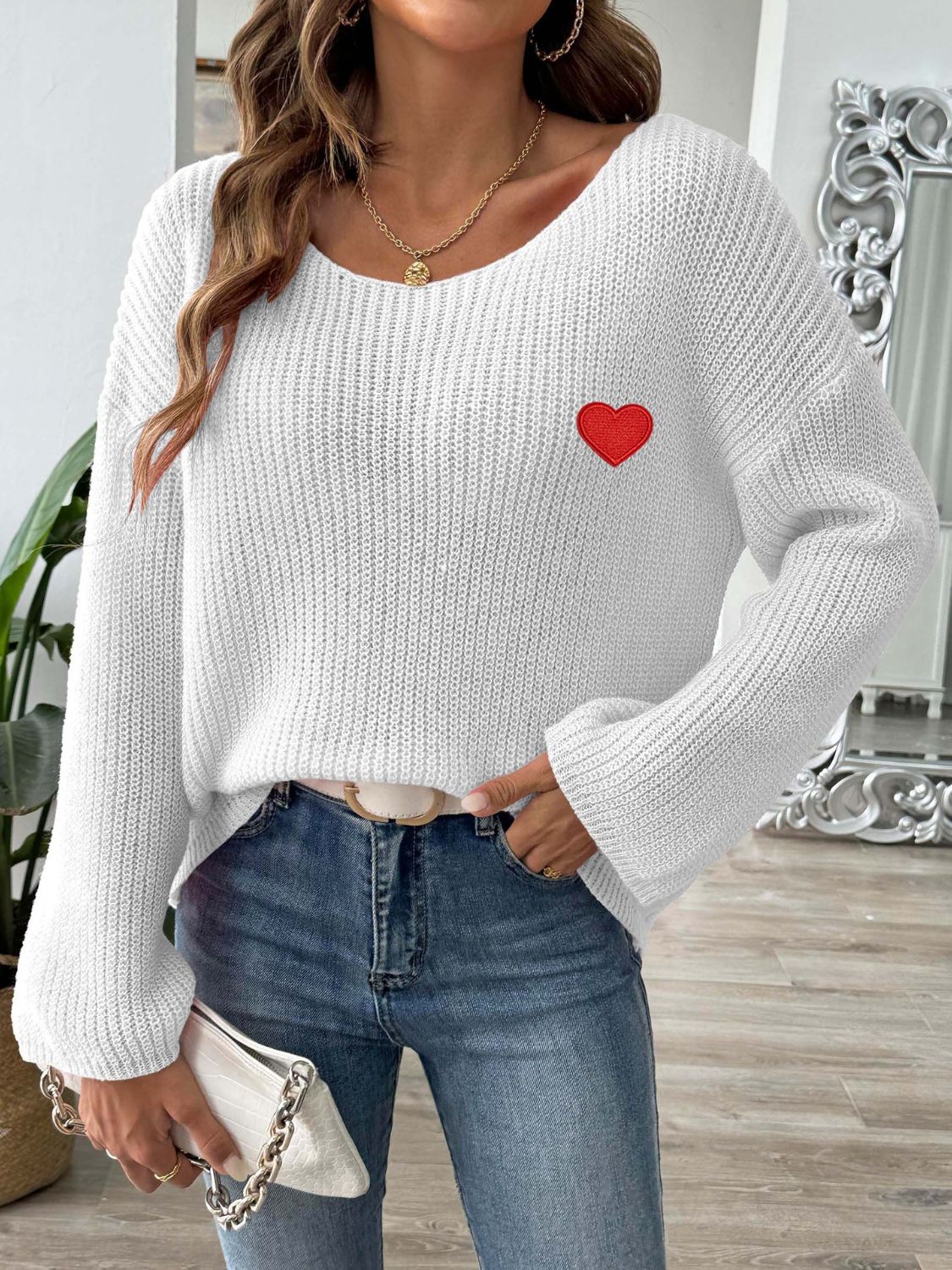 White boatneck knit sweater with embroidered red heart detail.