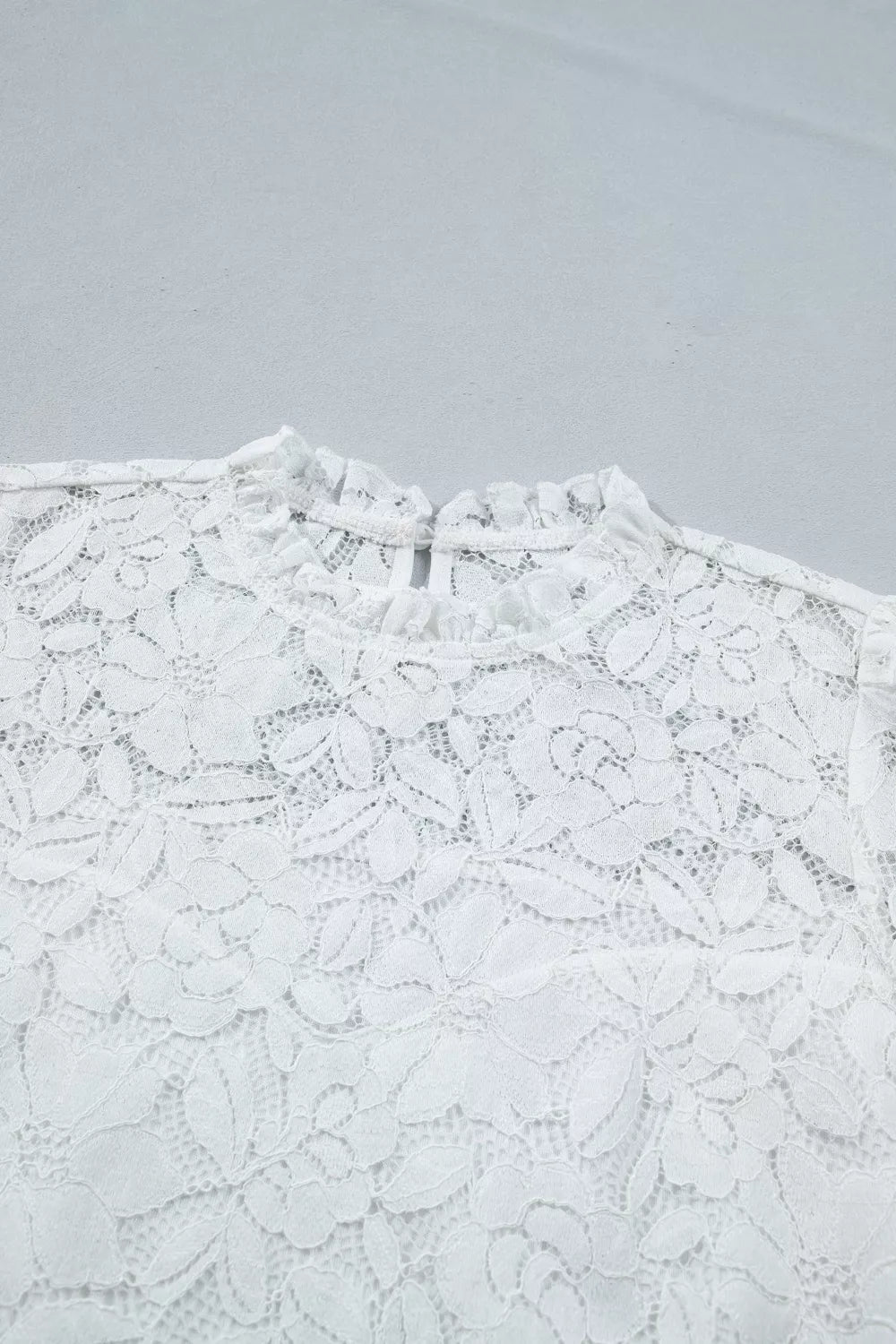 White lace blouse with ruffled mock neckline and floral pattern.