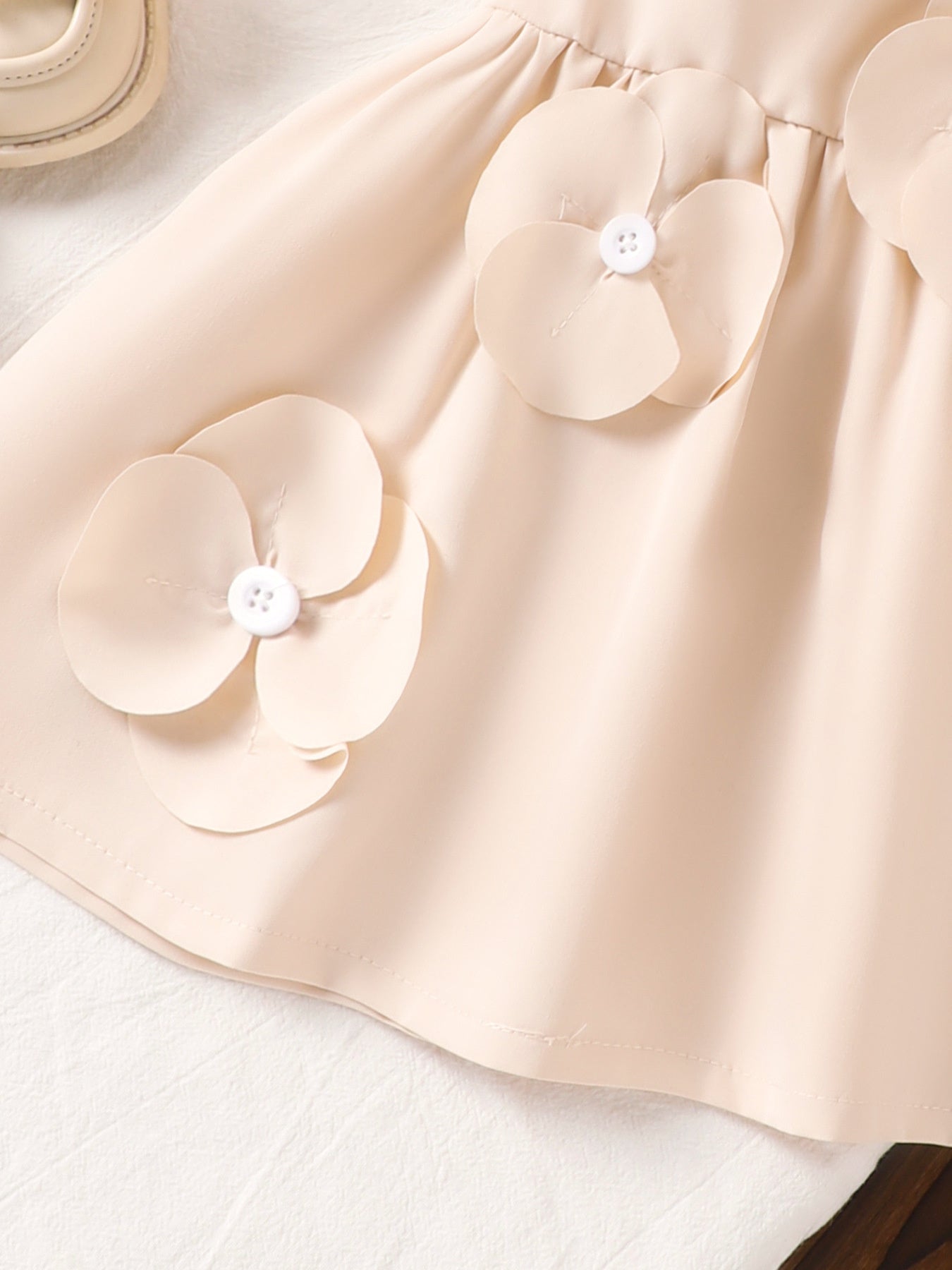 Off-white baby dress with 3D flower appliqués and white buttons.