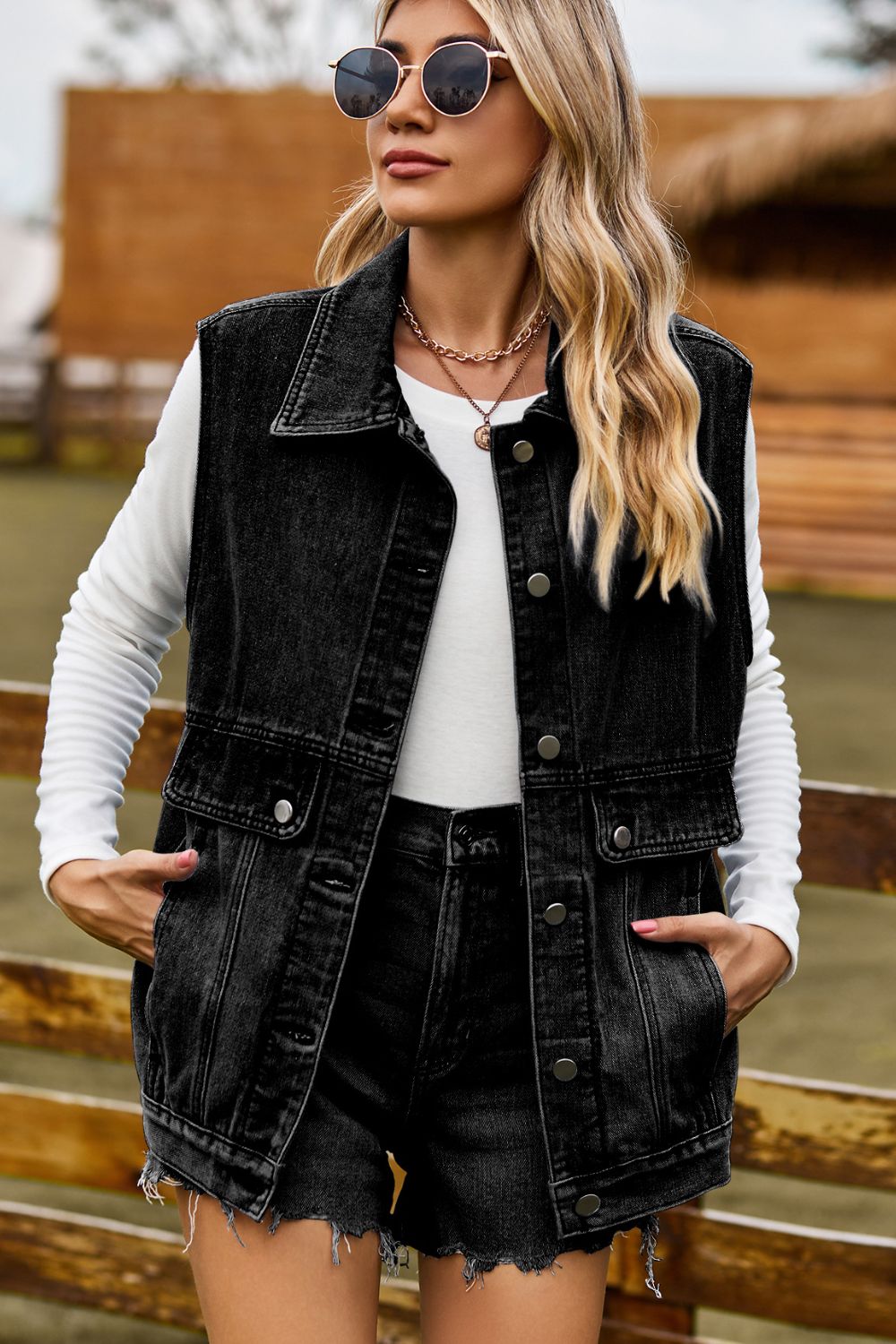 Sleeveless dark denim utility vest with button front and chest pockets.
