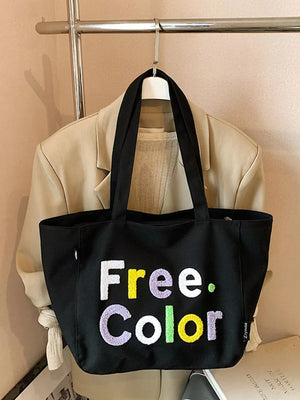Black canvas shoulder bag with embroidered "Free. Color" text in vibrant letters.