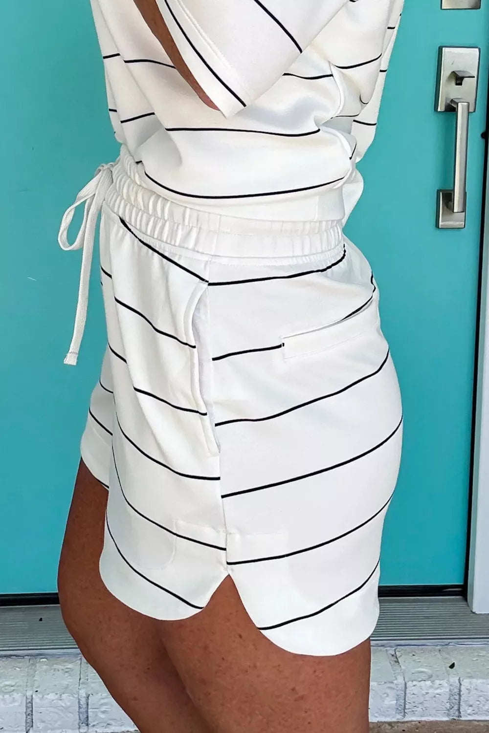 White polyester bikini shorts with black stripes, drawstring waist, and side pockets.