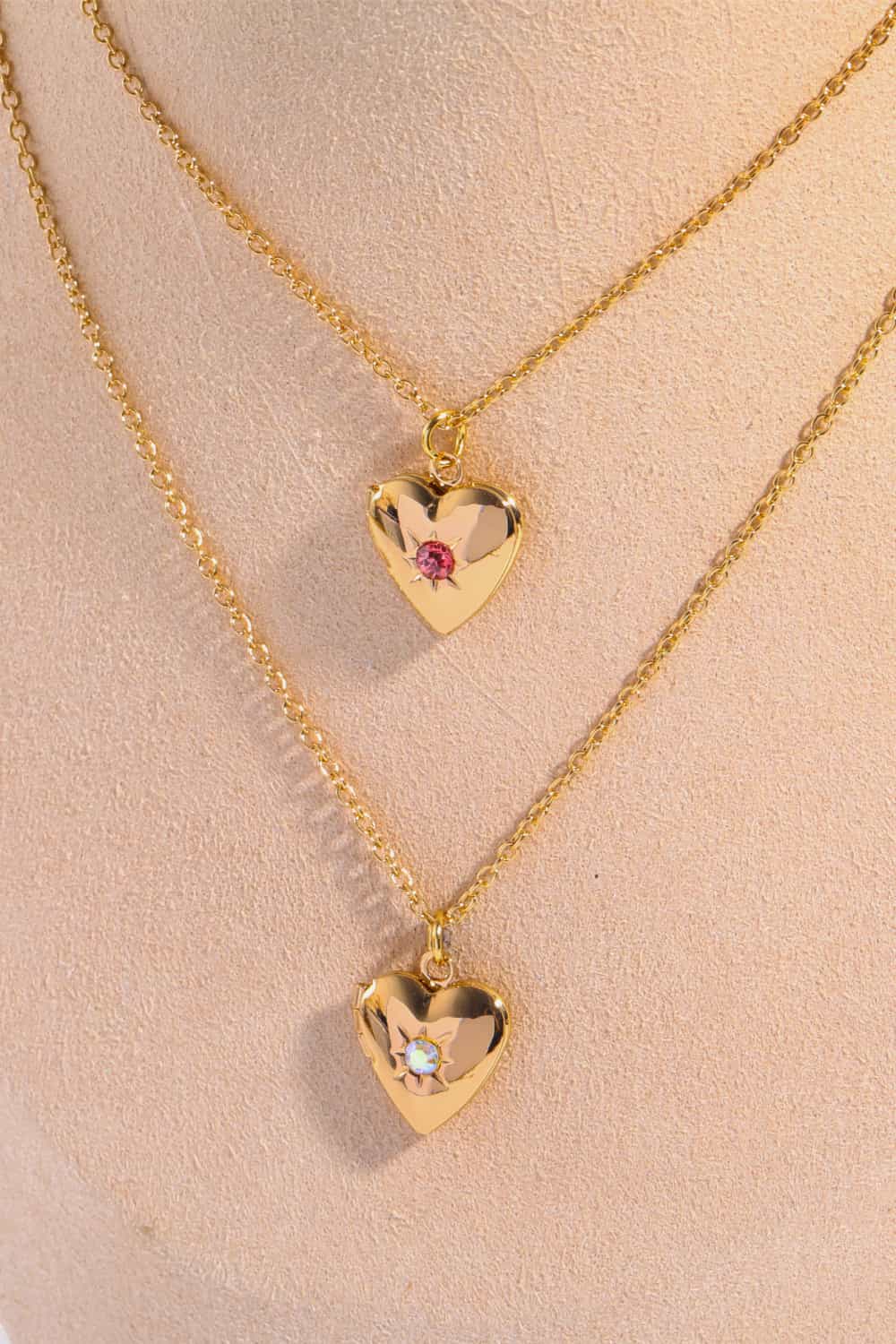 Gold heart locket necklaces with gemstone accents, one with a pink gemstone, the other with a clear gemstone.