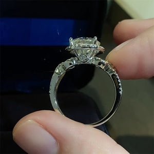 Silver halo moissanite engagement ring with twisted band and pavé diamonds.