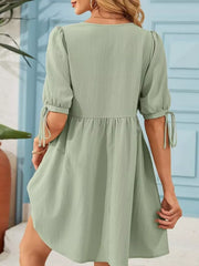 Light green mini dress with puff sleeves and tie details, tiered skirt.
