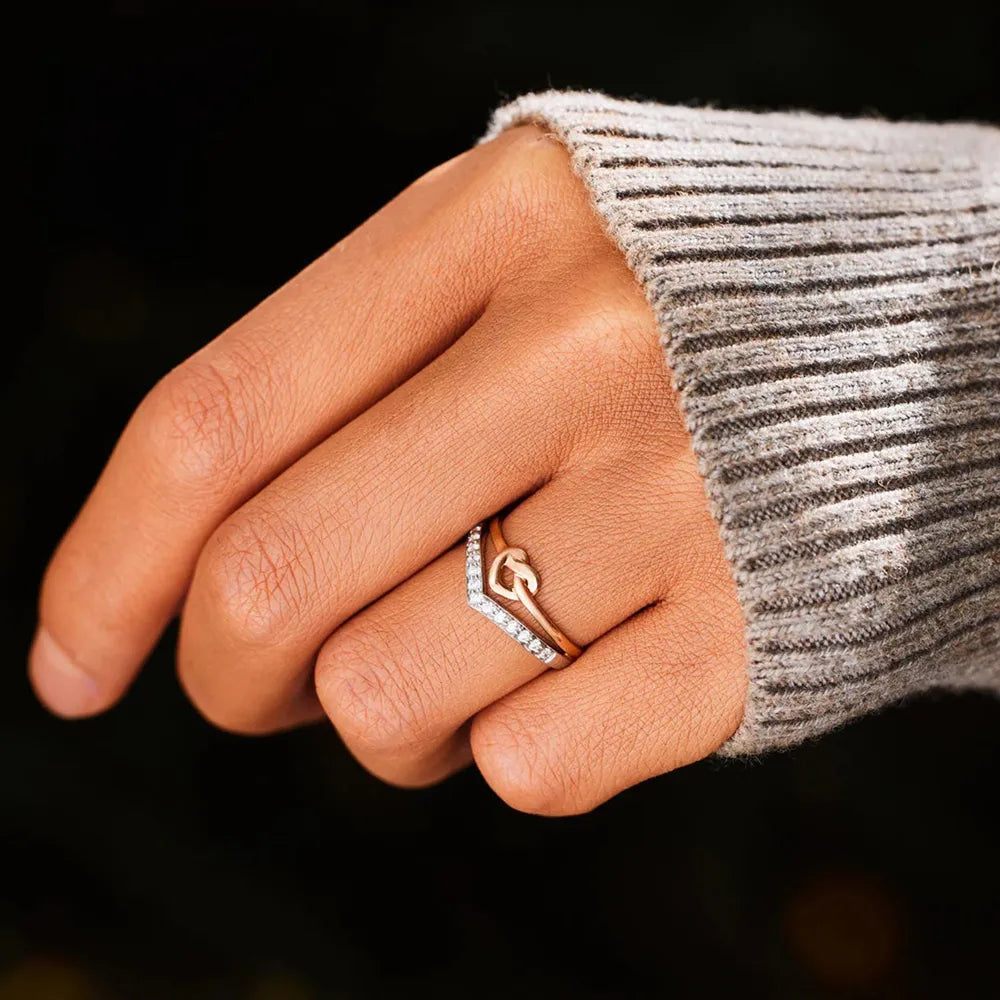 Silver knot and chevron rings with cubic zirconia accents stacked on a finger.