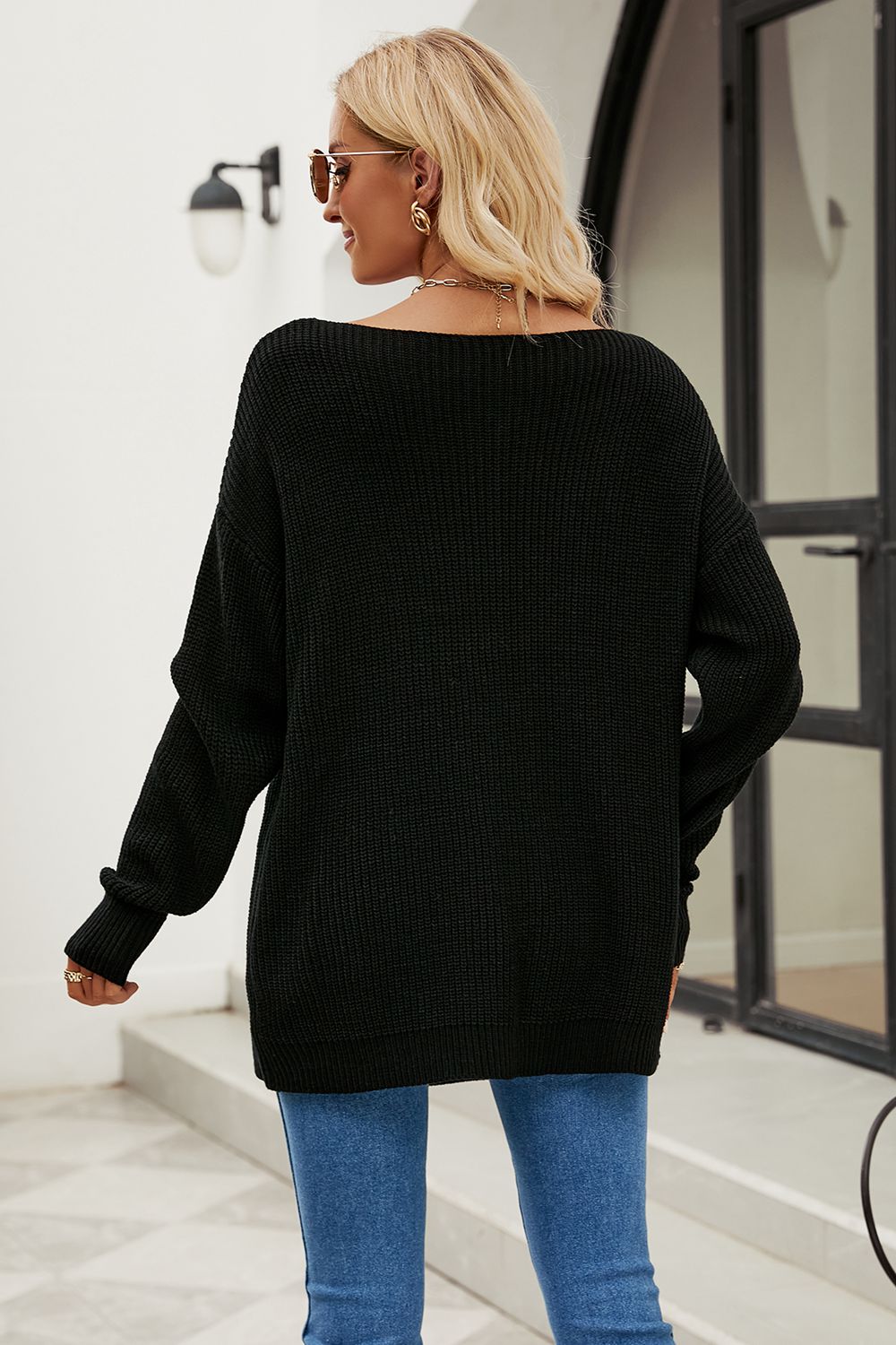 Black off-the-shoulder distressed knit sweater with boat neck and long sleeves.