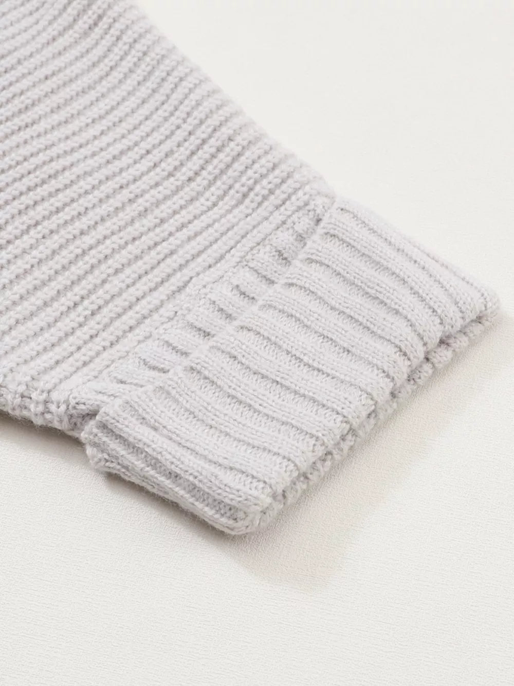 Light gray acrylic knit cardigan sleeve detail with ribbed cuff and textured knit.