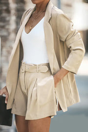 Camel double-breasted blazer and pleated shorts set with a white V-neck top and gold necklace.