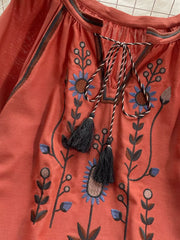 Orange red tie neck blouse with intricate floral embroidery and tassels.