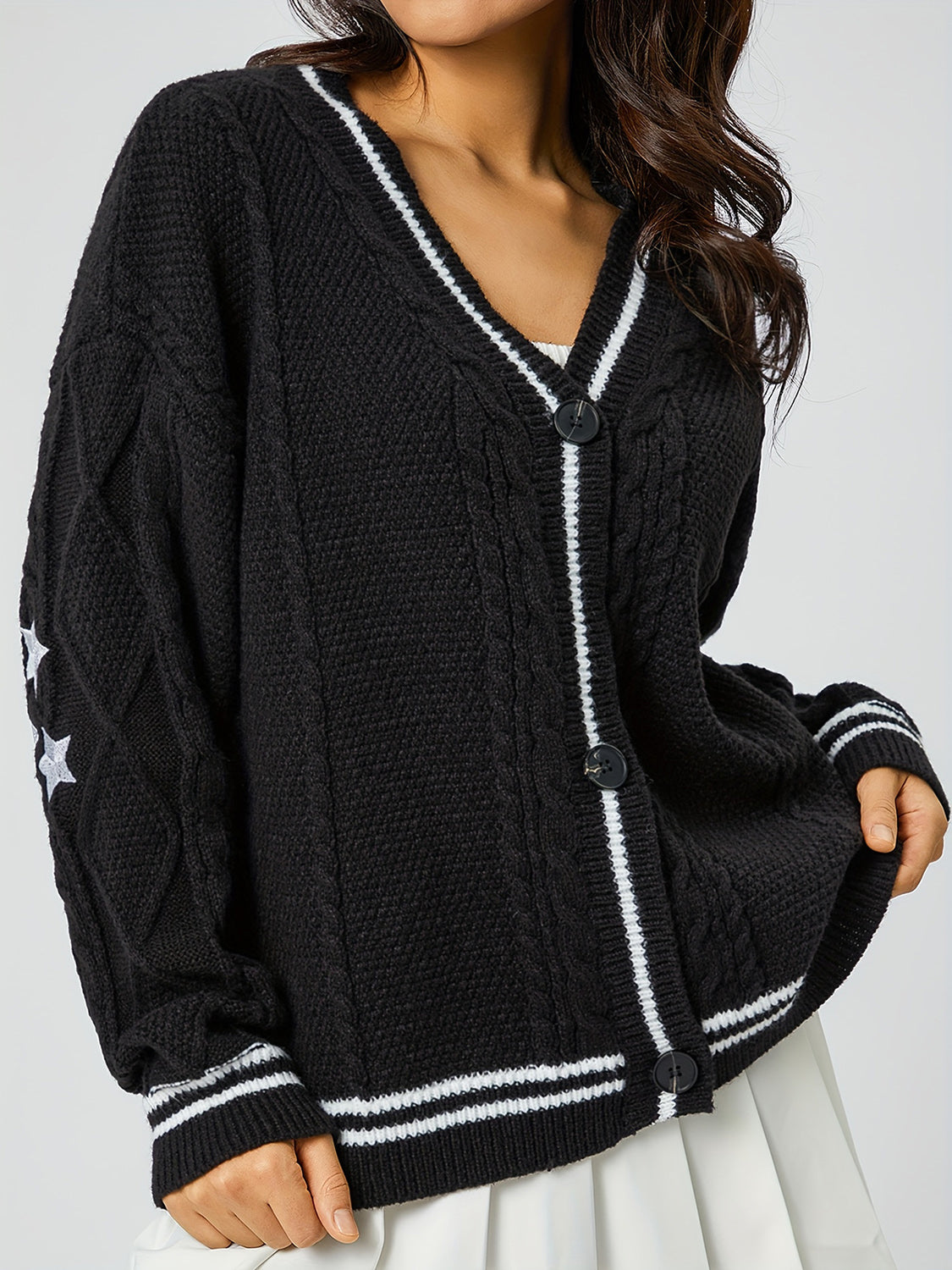 Black cable knit cardigan with white stripe trim and embroidered stars on sleeve.