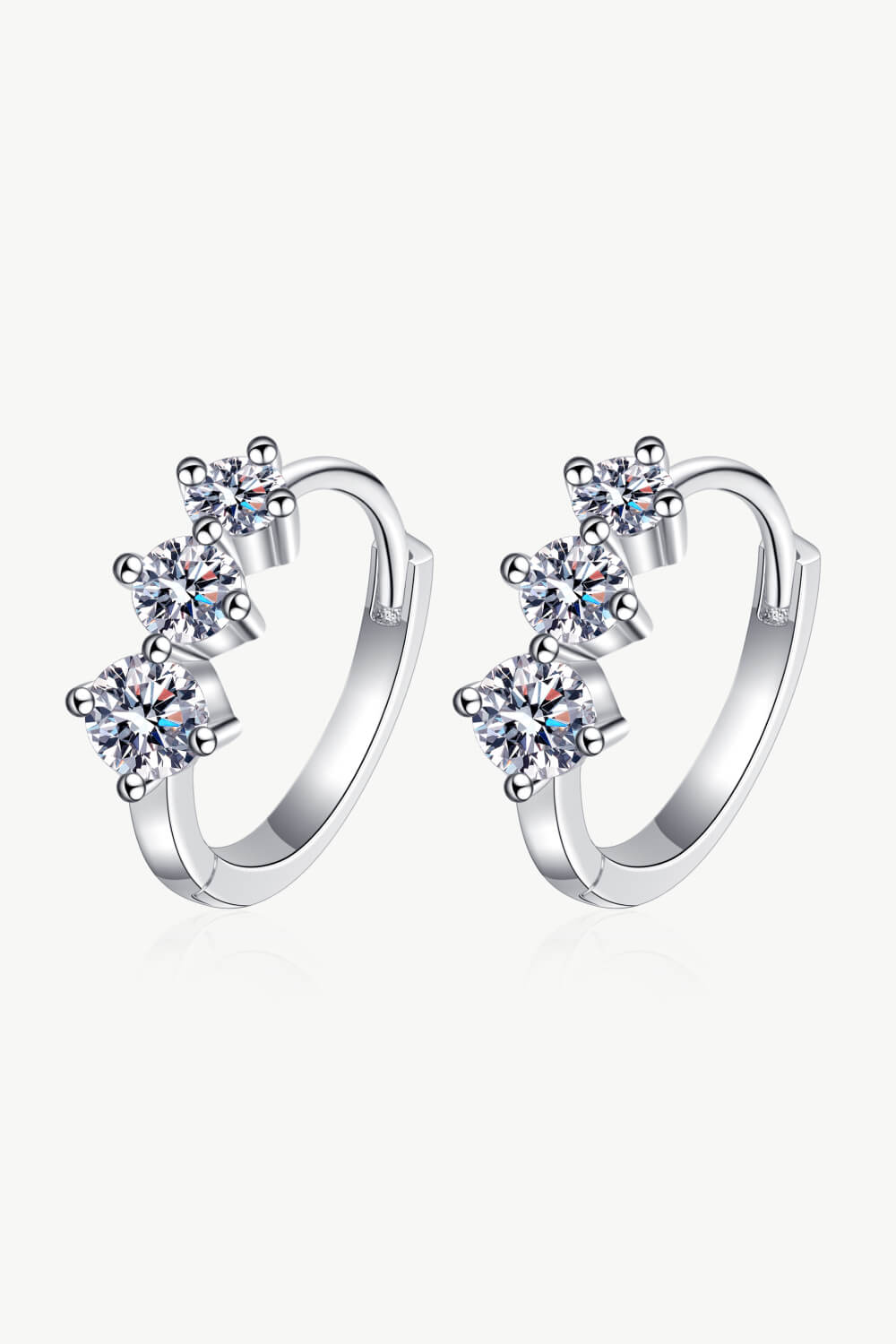 Silver huggie earrings with three clear cubic zirconia stones in a cluster design