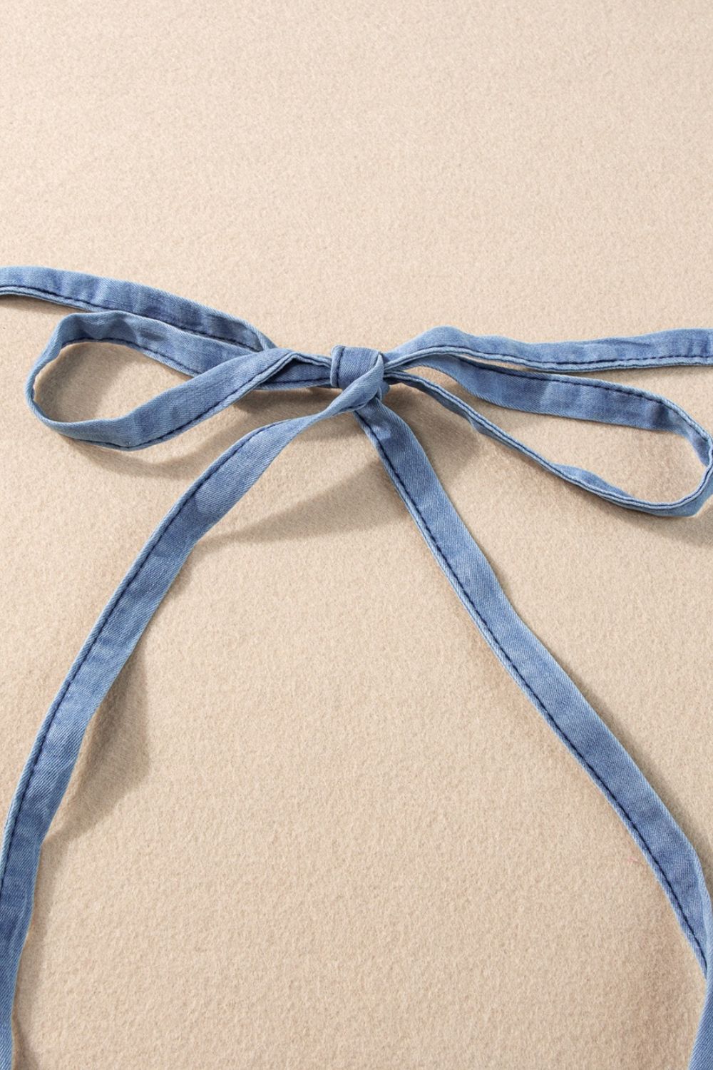 Denim romper with adjustable tie straps in medium wash.