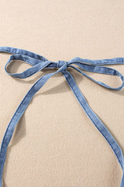 Denim romper with adjustable tie straps in medium wash.