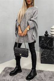 Gray knit sweater with cape sleeves, crew neck, and relaxed fit, styled with black pants and boots.