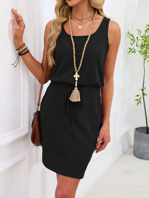 Sleeveless black waffle-knit drawstring dress with tassel detail and scoop neckline.