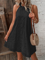 Black eyelet halter trapeze dress with scalloped hem, styled with a straw bag.