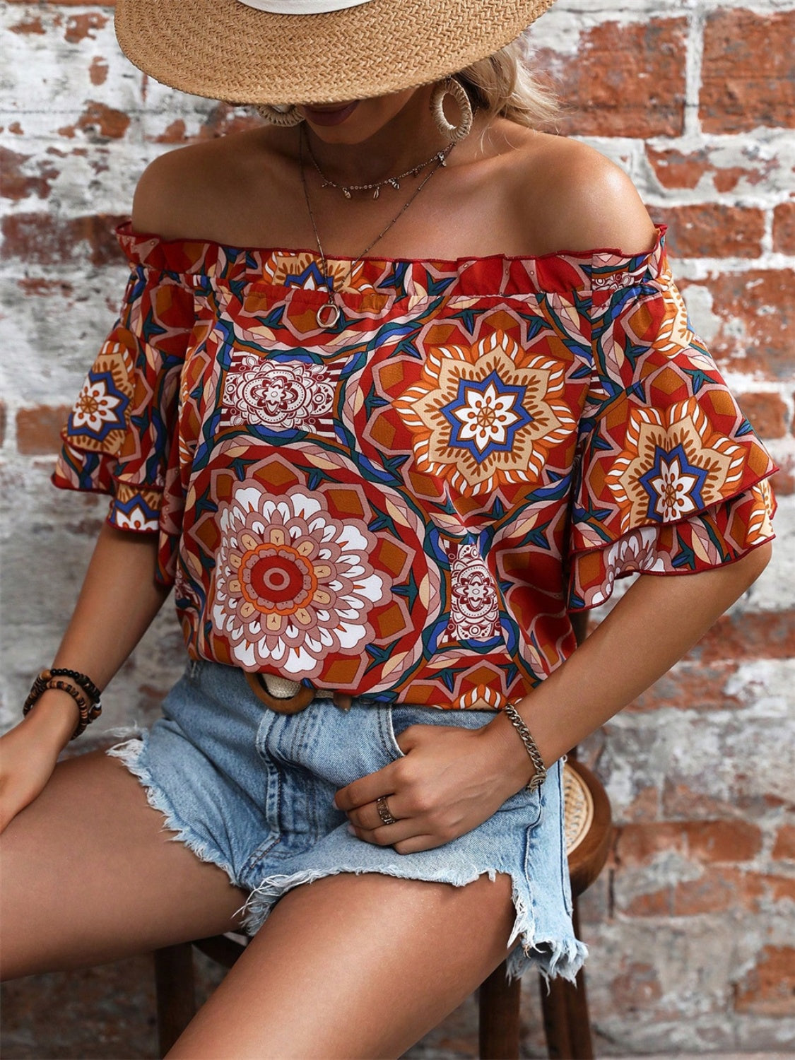 Bohemian ruffled off-shoulder blouse with bold print in terracotta, featuring tiered flutter sleeves.
