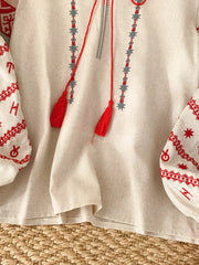 Cream folk-inspired tie neck shirt with red embroidery and tassels.