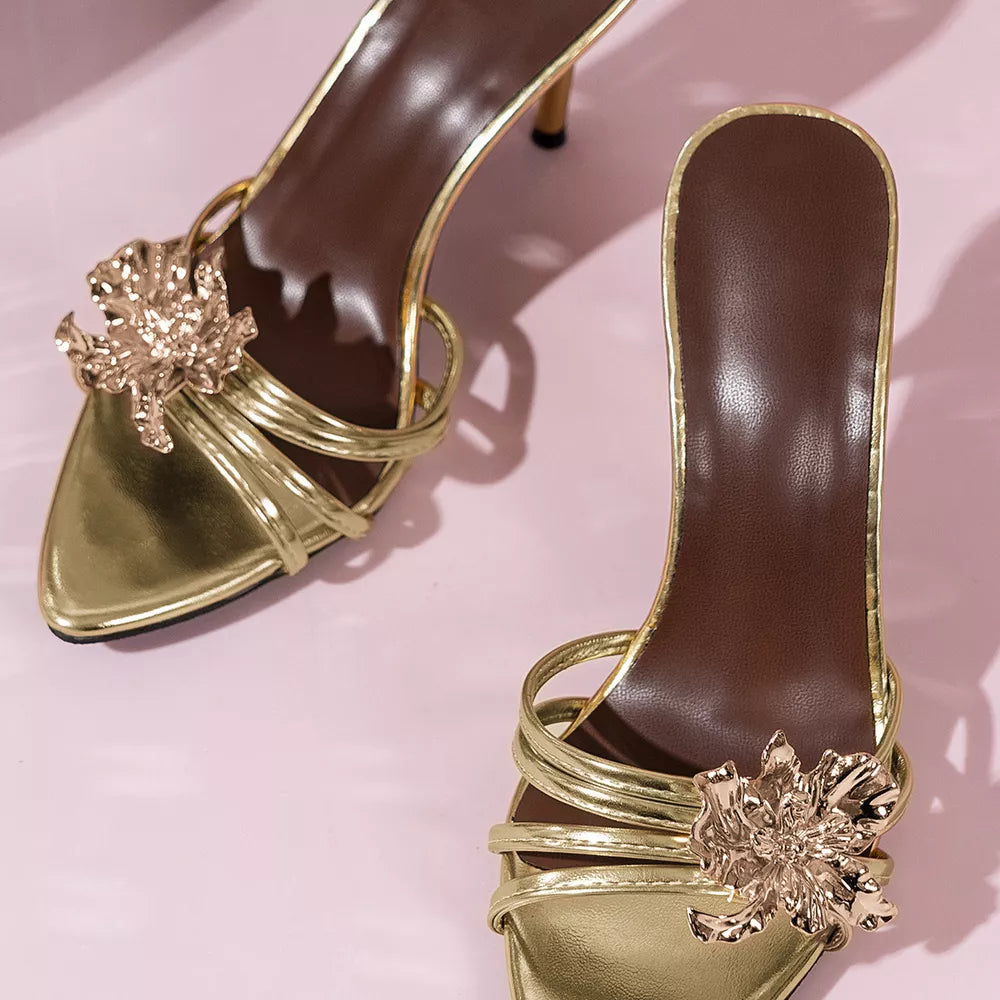 Gold high heel sandals with delicate straps and a floral embellishment.
