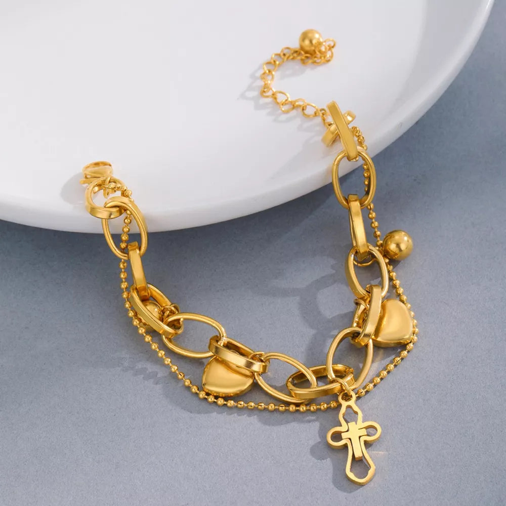 Gold charm bracelet with cross and heart charms, featuring layered chains and bead accents.