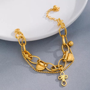 Gold charm bracelet with cross and heart charms, featuring layered chains and bead accents.