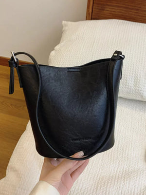 Distressed vintage bucket crossbody bag in black with adjustable strap and subtle embossed logo.