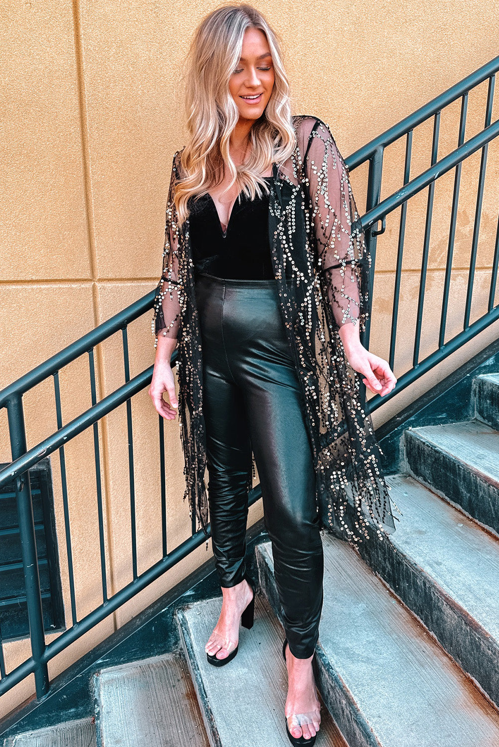Black sequin duster with flared sleeves and fringe detail, worn over a black velvet bodysuit and faux leather pants.
