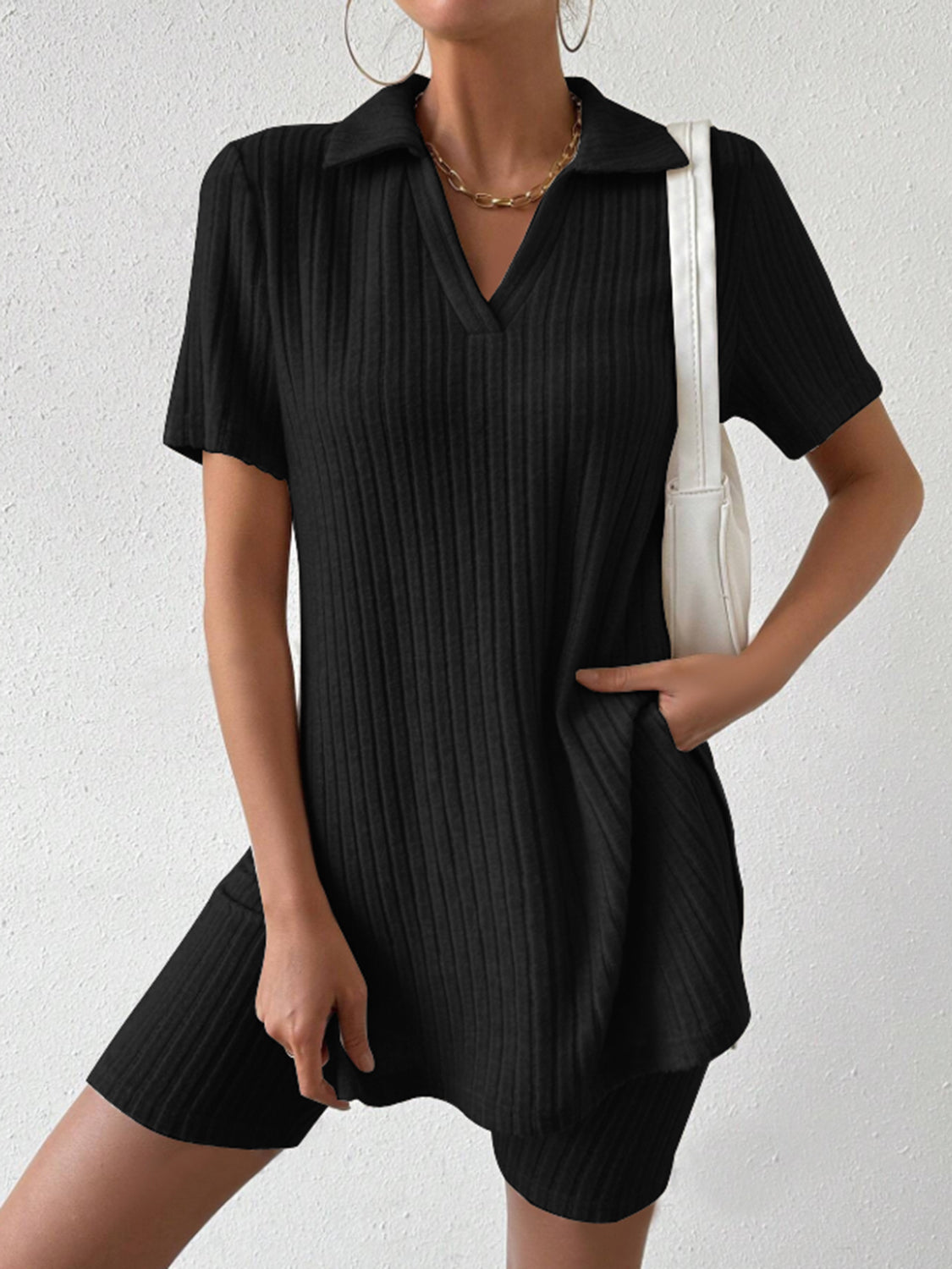 Black ribbed polo shirt and shorts set with a V-neck and collar, styled with a white bag.