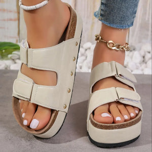 Beige platform sandals with double buckle straps and gold stud details.