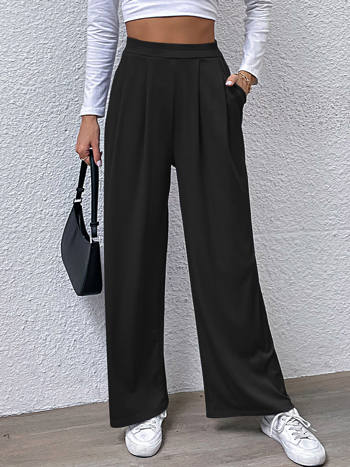 Black wide leg trousers with pleated front and pockets, styled casually.
