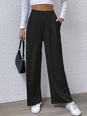 Black wide leg trousers with pleated front and pockets, styled casually.