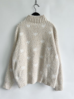 Textured acrylic turtleneck sweater in cream with a subtle heart motif pattern.