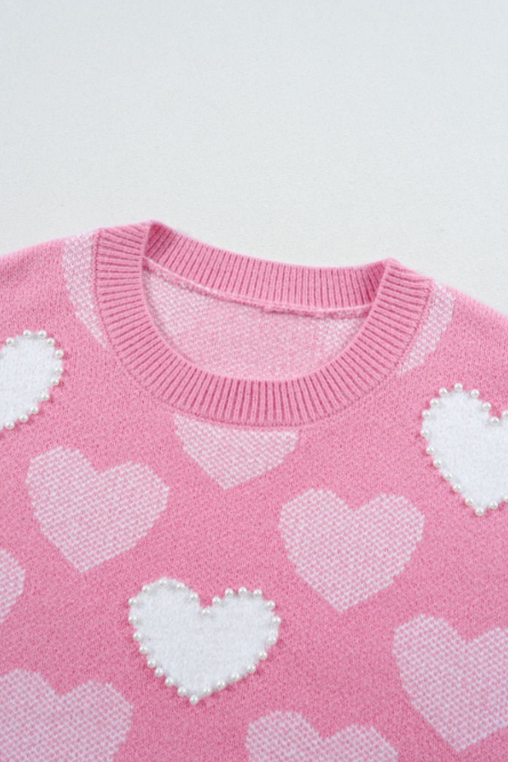 Pink knit sweater with white intarsia hearts and pearl embellishments.