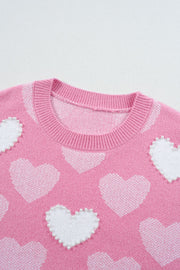 Pink knit sweater with white intarsia hearts and pearl embellishments.