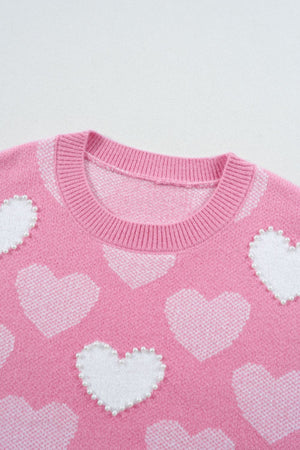 Pink knit sweater with white intarsia hearts and pearl embellishments.