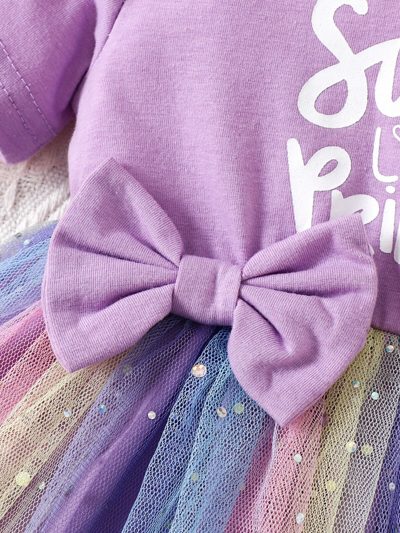 Lavender baby dress with rainbow tulle skirt, sequin accents, and a large bow detail.