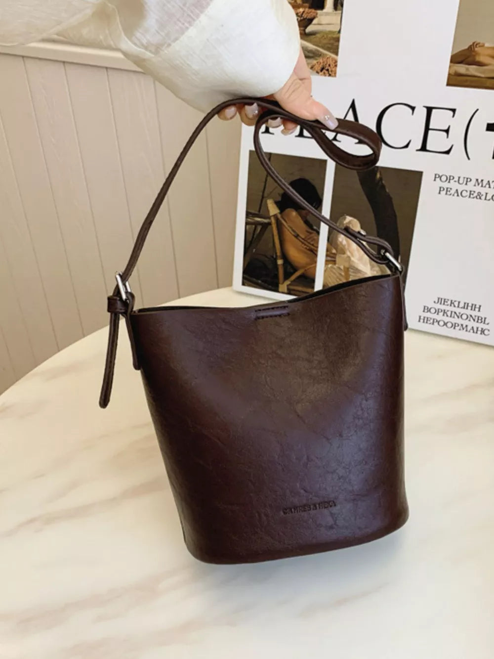 Brown distressed vintage bucket crossbody bag with adjustable strap and embossed logo.