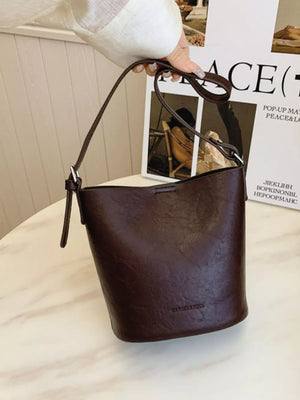 Brown distressed vintage bucket crossbody bag with adjustable strap and embossed logo.