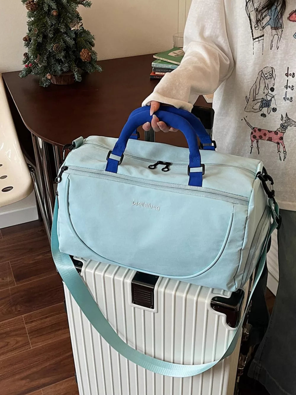 Light blue duffel bag with blue handles and strap, front zip pocket, and adjustable strap.