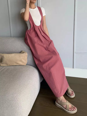 Elegant pleated overall dress in dark pink with pockets, styled with a white tee and sandals.
