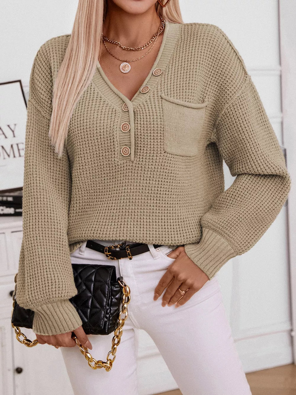 Relaxed knit sweater with V-neck, button placket, and chest pocket in a neutral color.
