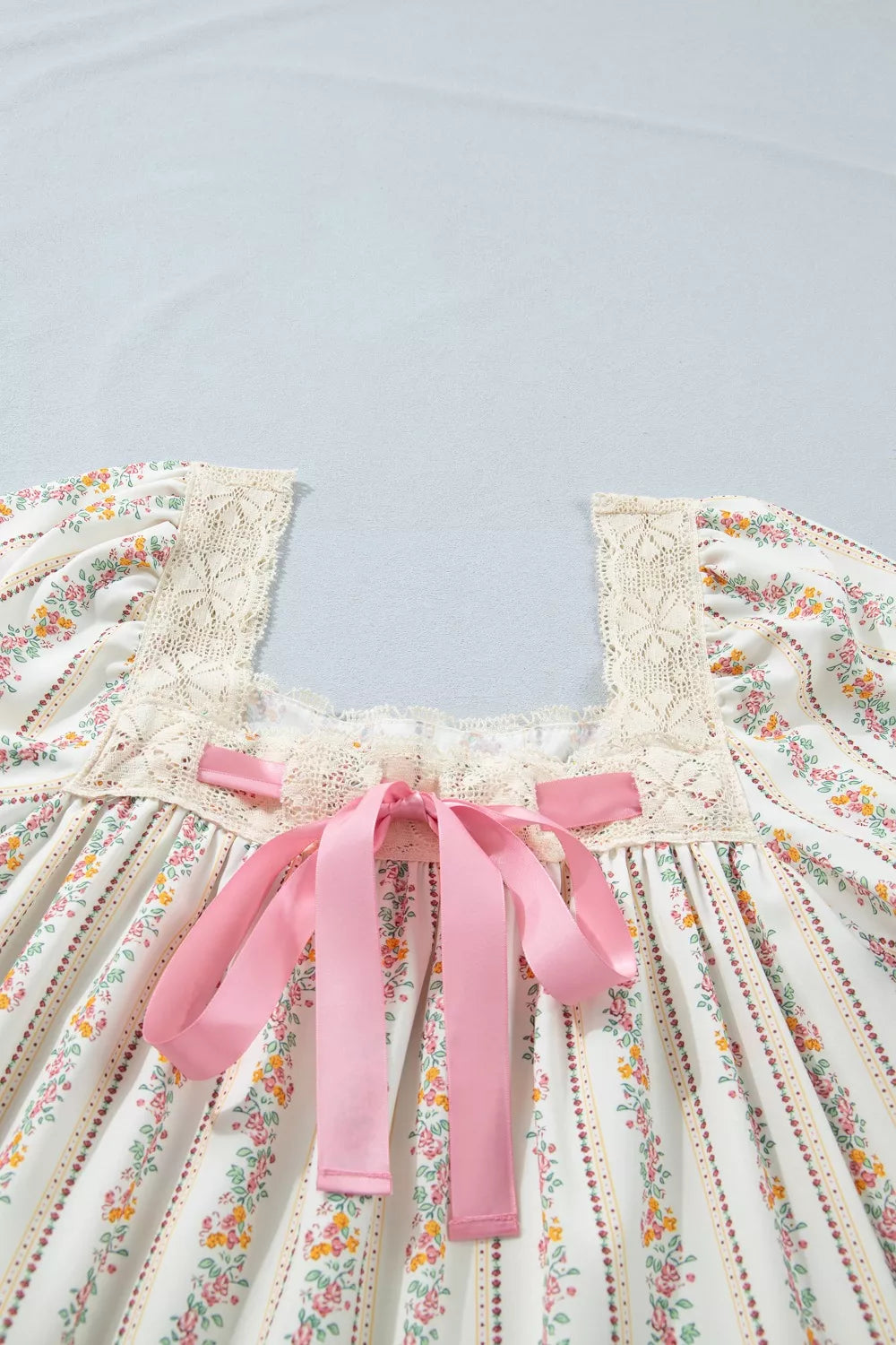 Floral mini dress with lace trim, square neck, pink bow detail, and puff sleeves.